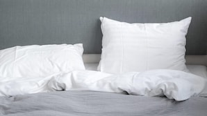 Un lit avec une literie blanche et une tête de lit grise.