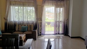 Een woonkamer met een bank, een televisie en uitzicht op een gebouw door een raam.