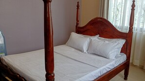 Een kamer met een hemelbed met witte beddengoed, een raam en gordijnen.