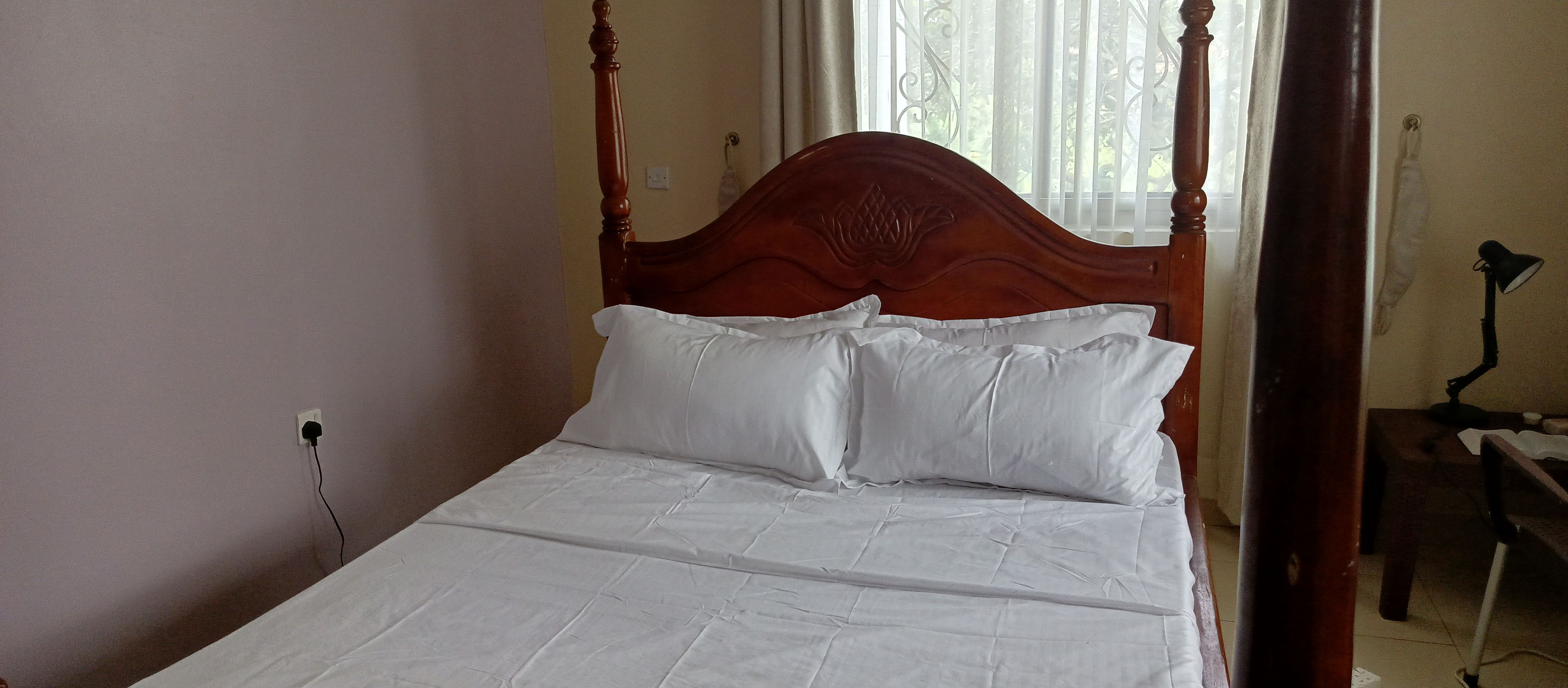 Ein Bett mit Holz-Kopfteil, weißer Bettwäsche und einer Steckdose an der Wand.