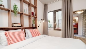 Habitación de hotel con una cama grande, cabecera de madera, una mesita de noche con lámpara, ventana con cortinas y vistas al exterior.