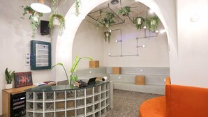 A reception area with a curved glass desk, a wooden cabinet, and an orange couch. - Dogpound Athens (Athens)