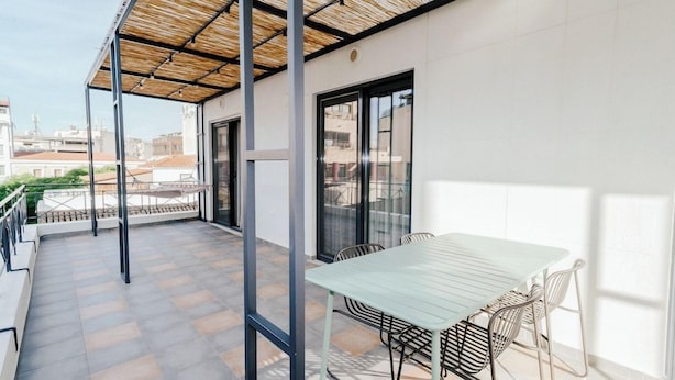 Un balcón con mesa y sillas, una pérgola y vistas a la ciudad.