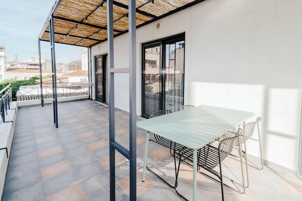 A balcony with a table and chairs, a pergola, and a view of the cityscape.