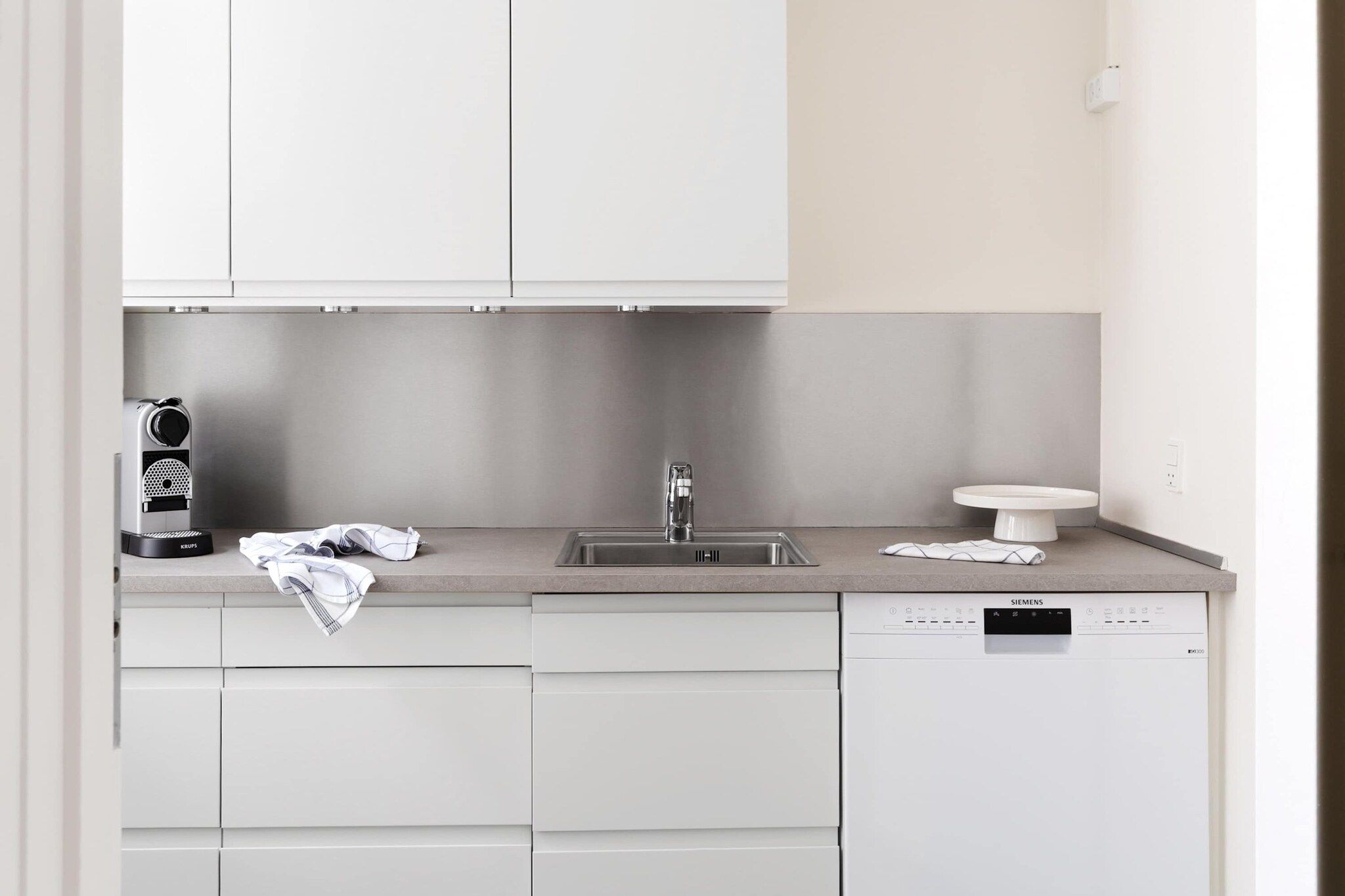 A modern kitchen with white cabinetry, a built-in dishwasher, and a coffee maker.