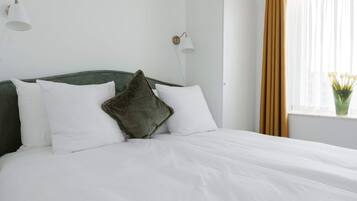 Una cama bien tendida con sábanas blancas, cabecera verde y dos lámparas fijadas a la pared.
