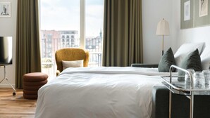 Ein Hotelzimmer mit Bett, Sessel, Schreibtisch und einem fenster mit Vorhängen.