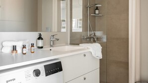 Ein modernes Badezimmer mit einem weißen Waschtisch, einem großen Spiegel, einer Dusche mit Duschbrause und einer integrierten Seifenspender.