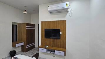 Quarto com guarda-roupa, televisão fixada em um painel de madeira e ar-condicionado.