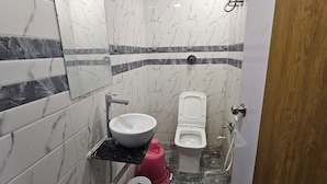 A bathroom with a marble-tiled wall, a white sink, a toilet, and a red fire extinguisher. - Hotel Orion  (Gandhinagar)