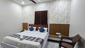 A hotel room with a bed, a nightstand, a chair, and a patterned wallpaper. - Hotel Orion  (Gandhinagar)