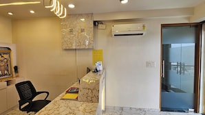 A reception desk with a marble counter, a black office chair, and a wall-mounted air conditioner. - Hotel Orion  (Gandhinagar)