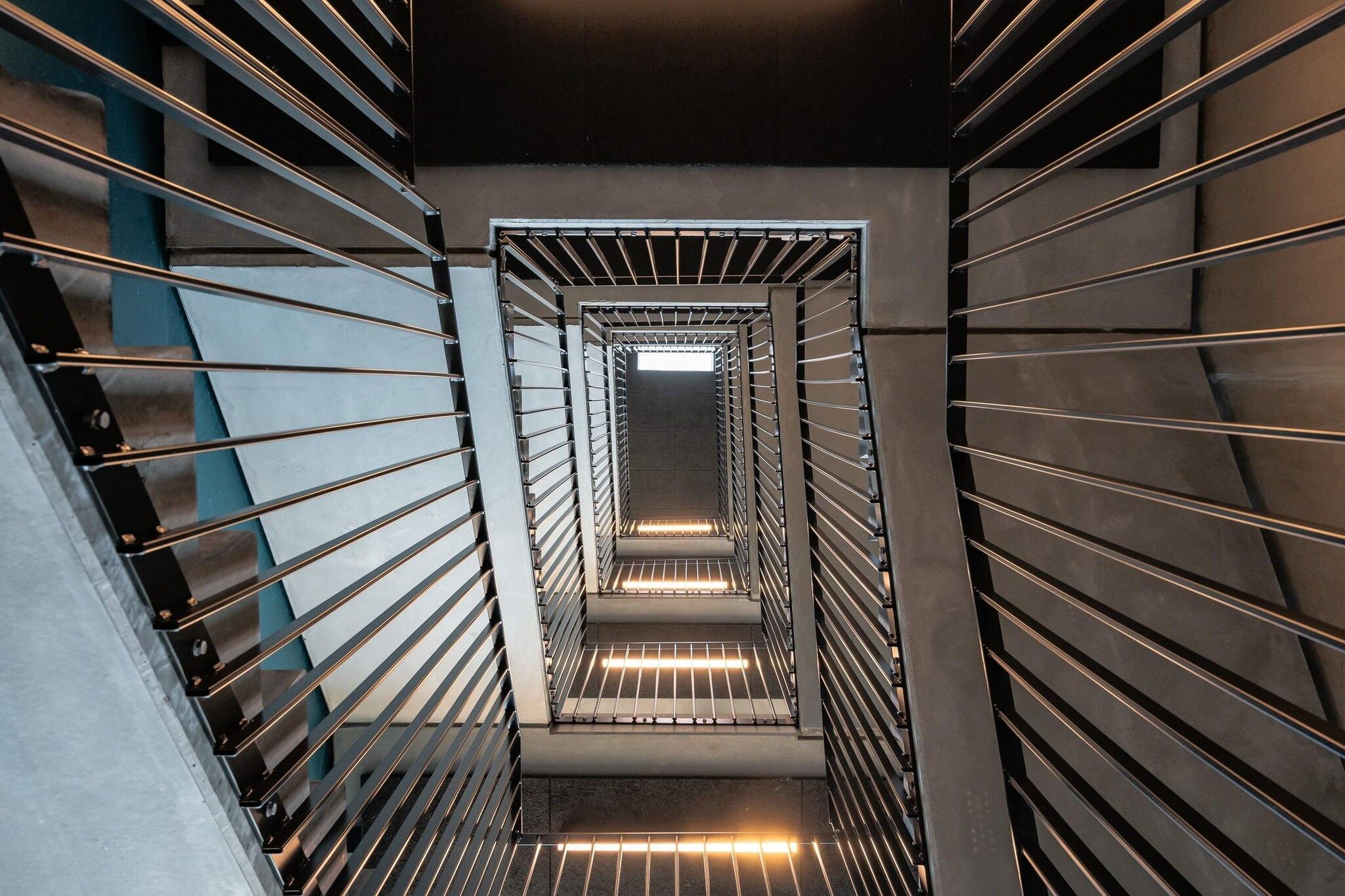 Una escalera moderna, cerrada, con barandillas de metal y un candelabro en el centro.
