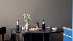 Une table ronde avec un vase de fleurs, deux bouteilles de bière, une canette de soda, un verre de bière, un bol et une planche en bois avec des dés.