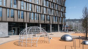 Un bâtiment moderne doté d’une façade à motifs géométriques et d’une aire de jeux comprenant une structure en forme de dôme et des sculptures métalliques.
