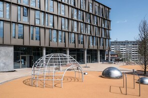 Ein modernes Gebäude mit einem Raster aus Fenstern und einem Spielbereich mit einer kuppelförmigen Struktur und Metallskulpturen.