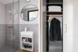 Ein modernes Badezimmer mit einer Duschkabine aus Glas, einem weißen Waschbecken mit Pflegeprodukten und einem Spiegel.