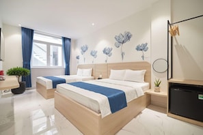 Une chambre d’hôtel avec deux lits, un petit bureau, un réfrigérateur et un mur décoré d’œuvres d’art florales.