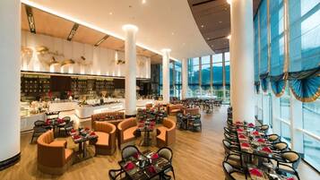 A spacious hotel lobby with a central bar area, multiple seating arrangements, and large windows providing natural light.