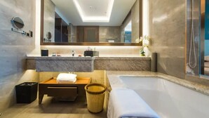 Ein modernes Badezimmer mit einem großen Spiegel, einer Badewanne, einer hölzernen Sitzbank und einem Mülleimer.