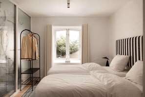 Ein Schlafzimmer mit einem Bett, einem Fenster, einem Kleiderständer und Blick ins Grüne.