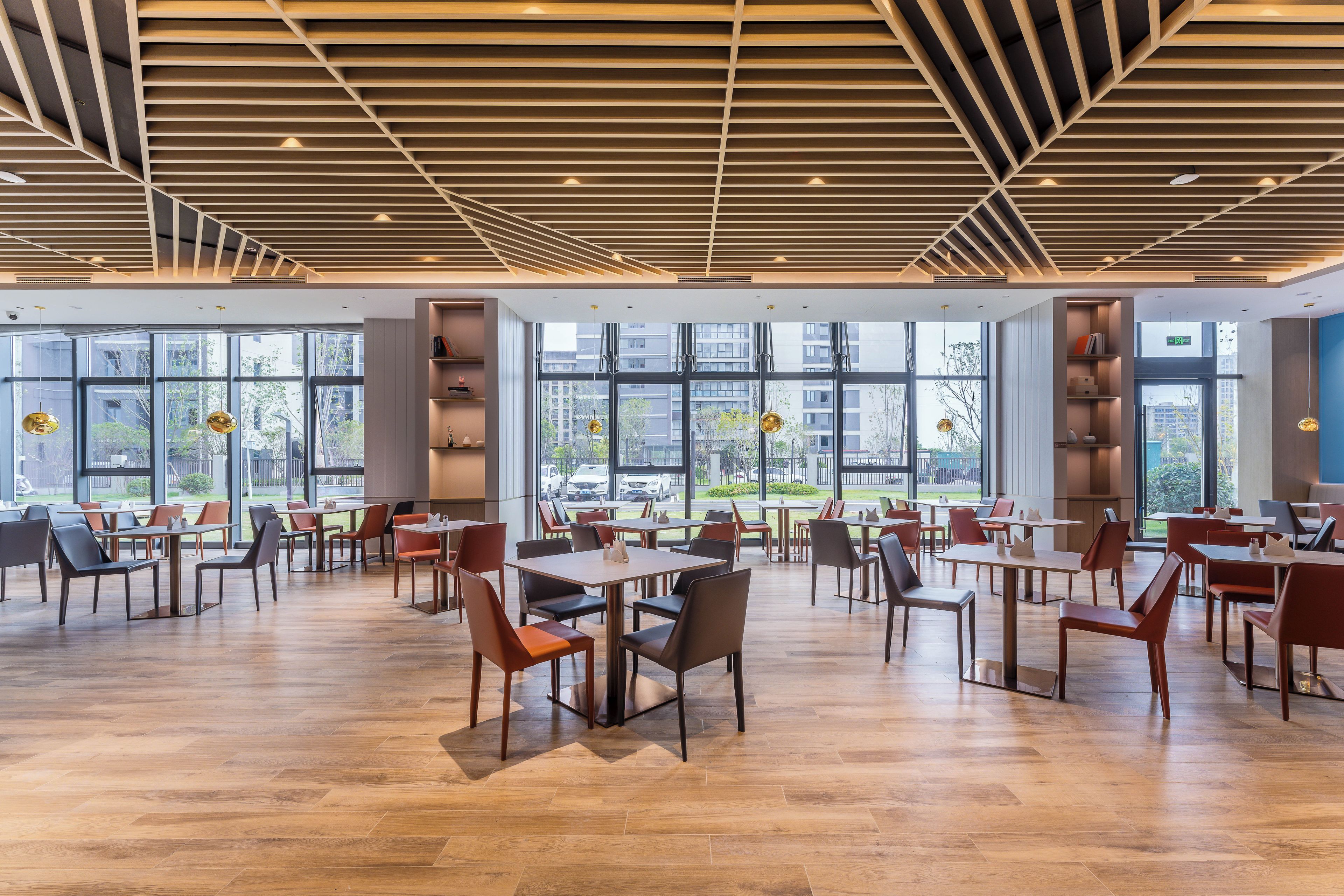 A spacious indoor area with tables and chairs, large windows, and a wooden ceiling.