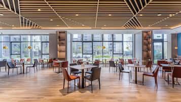 A spacious indoor area with tables and chairs, large windows, and a wooden ceiling.
