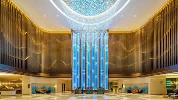 A spacious lobby with a high ceiling, a central column with vertical lighting, and a reception desk.