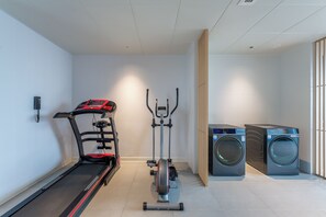 Un gimnasio con una cinta de correr, una elíptica y dos lavadoras.