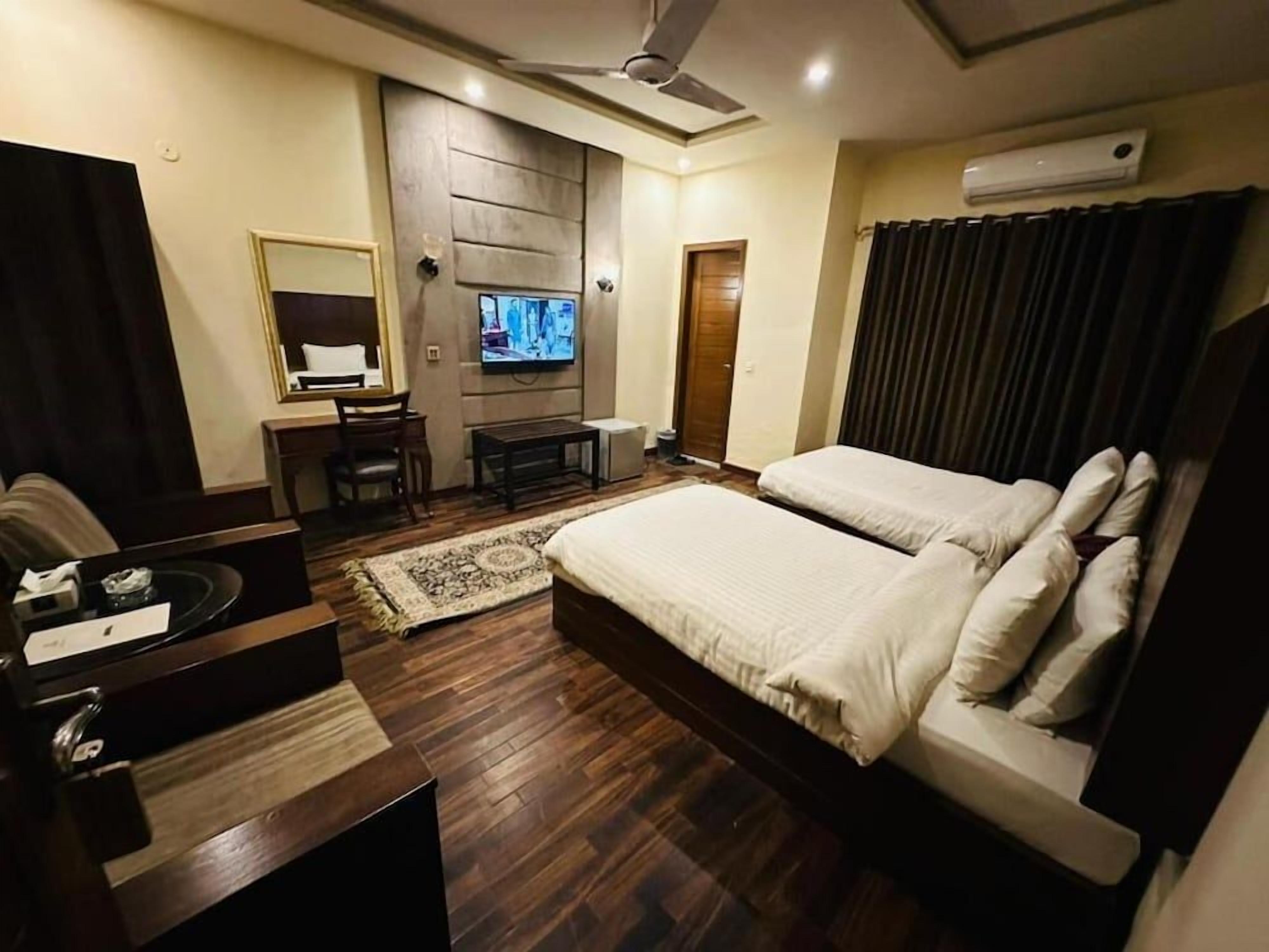 A hotel room with a bed, a desk, a television, and a ceiling fan.