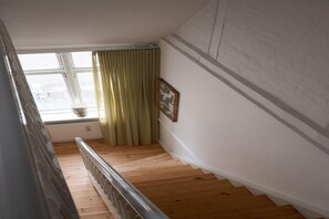 A wooden staircase with a handrail, a window with curtains, and a framed picture on the wall. - Stay Near Tivoli and Stroget (København)