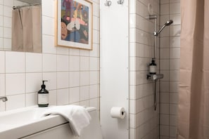 Et badeværelse med bruser, toilet, vask og et billede i ramme på væggen.