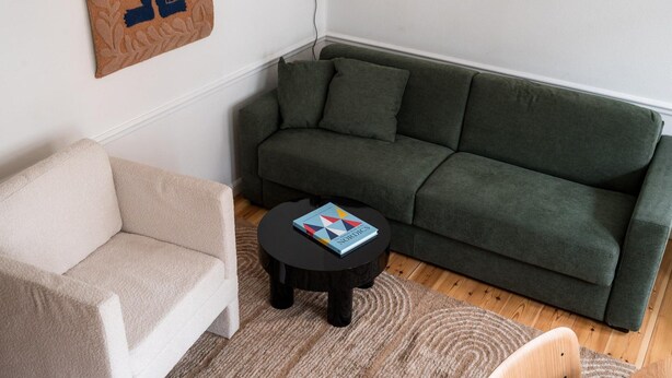 Ein Wohnzimmer mit einem grünen Sofa, einem beigen Sessel und einem kleinen schwarzen Tisch mit einem Buch.