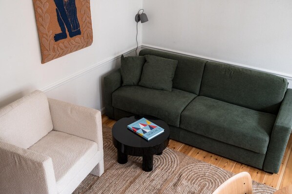 En stue med en grøn sofa, en beige lænestol og et lille sort bord med en bog.