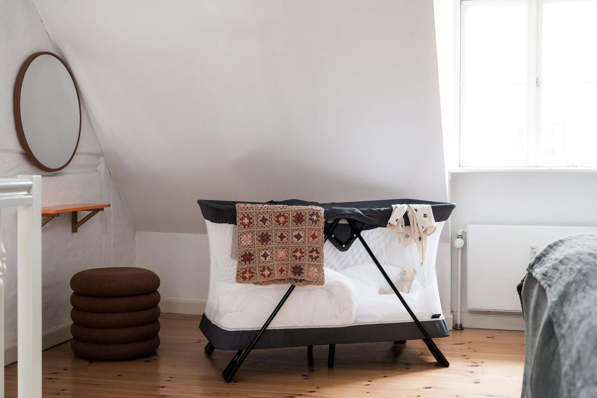 Une pièce avec un berceau, une petite table, un miroir et une fenêtre.