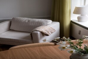 A corner of a room with a beige sofa, a small table with a vase of flowers, and a lamp on a bedside table. - Stay Near Tivoli and Stroget (København)