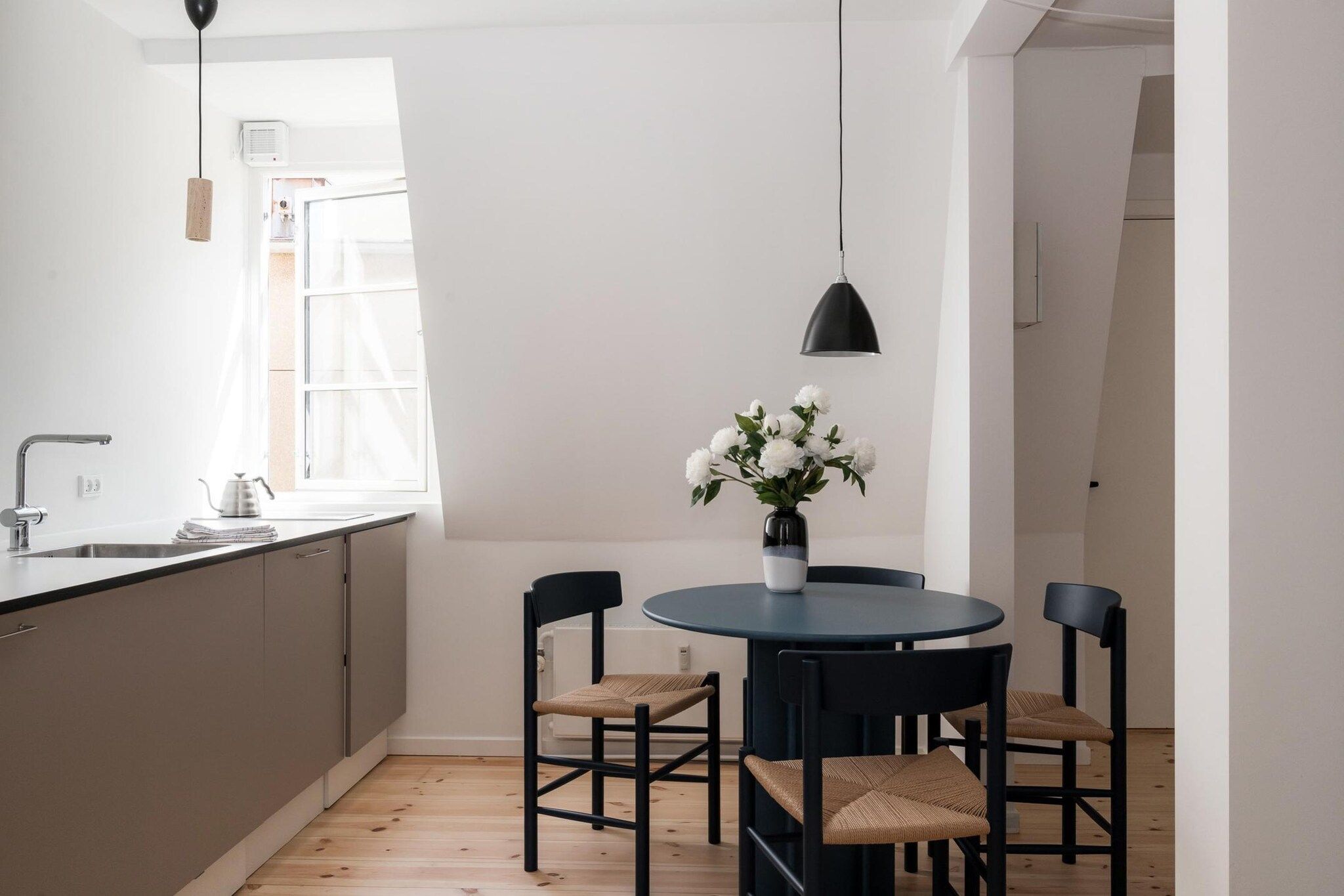 Et moderne køkken med et rundt bord, stole, et vindue og en hængende lampe.