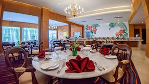 A hotel dining area with round tables, chairs, and a central bar. - Hotel Puri Senyiur (Samarinda)