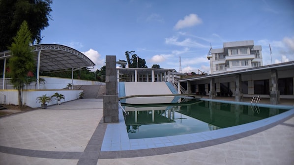 A swimming pool with a covered area, a staircase, and a building in the background. - Hotel Puri Senyiur (Samarinda)