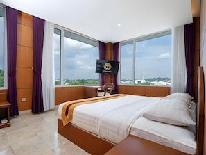 A hotel room with a large bed, a desk, and a TV mounted on the wall. - Hotel Puri Senyiur (Samarinda)