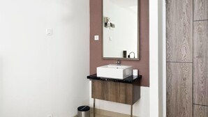 Une salle de bain avec un lavabo blanc, un miroir et une poubelle.