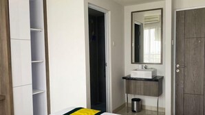 Une chambre à coucher comprenant un lit, une armoire, une salle de bain avec un lavabo et un miroir, et une porte donnant sur une autre pièce.
