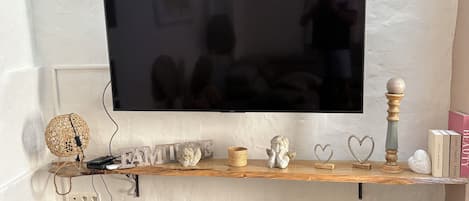 A flat-screen TV mounted on a wall with a wooden shelf below displaying decorative items, a wicker lamp, and a storage chest labeled 'Superior Los Angeles.'