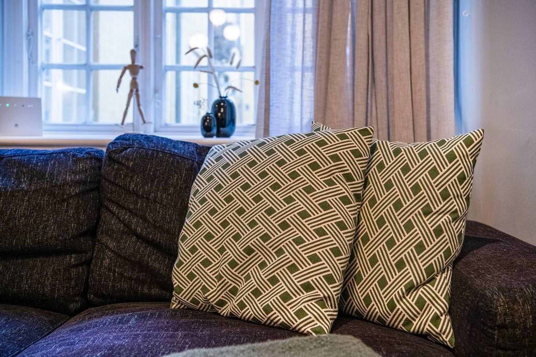 A sectional sofa with patterned cushions in a room with a window and a vase on a side table.