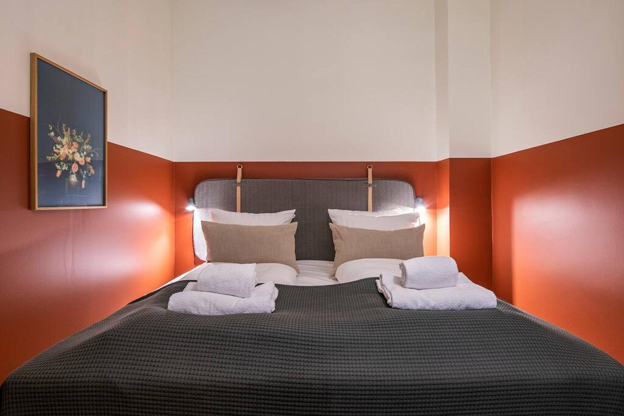 A hotel room with a bed, pillows, and a framed picture on the wall.