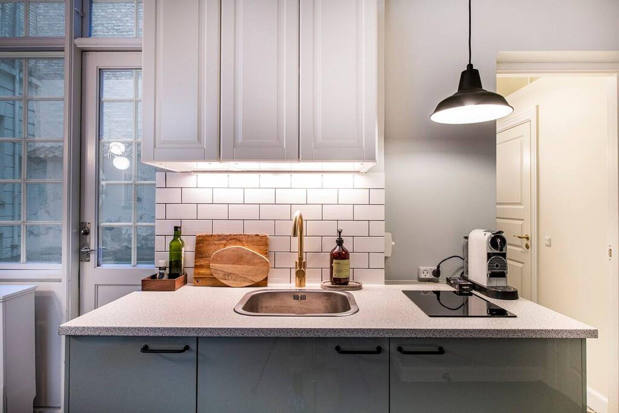 A kitchen with white cabinets, a stainless steel sink, a wooden cutting board, and a hanging pendant light.