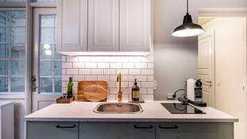 A kitchen with white cabinets, a stainless steel sink, a wooden cutting board, and a hanging pendant light.