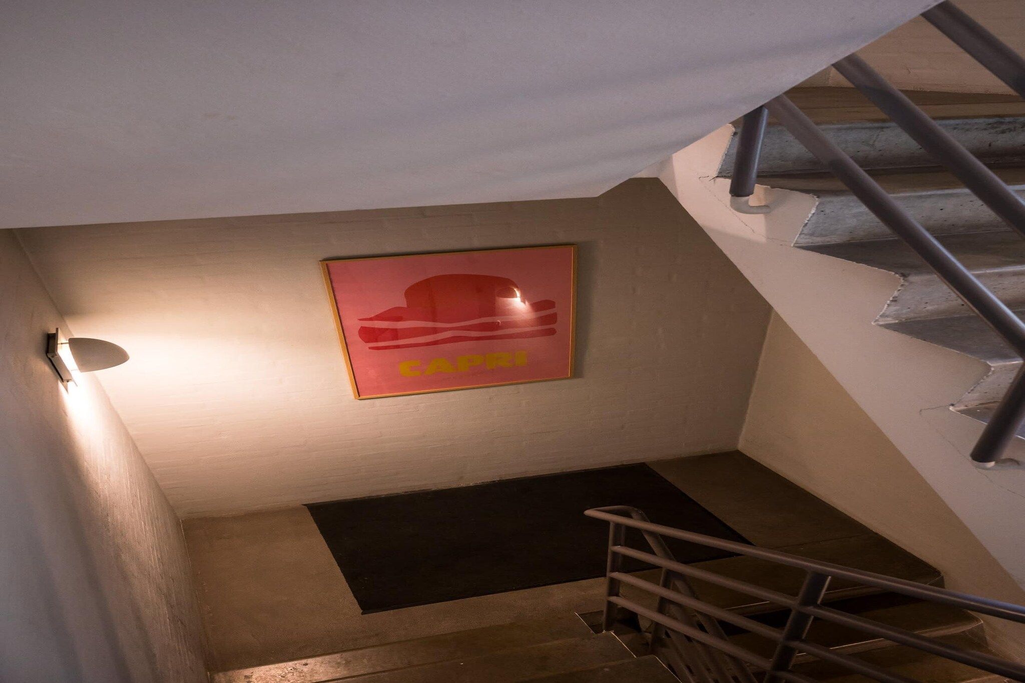 Eine Treppe mit Metallgeländer, einer Wandleuchte und einem gerahmten Poster.
