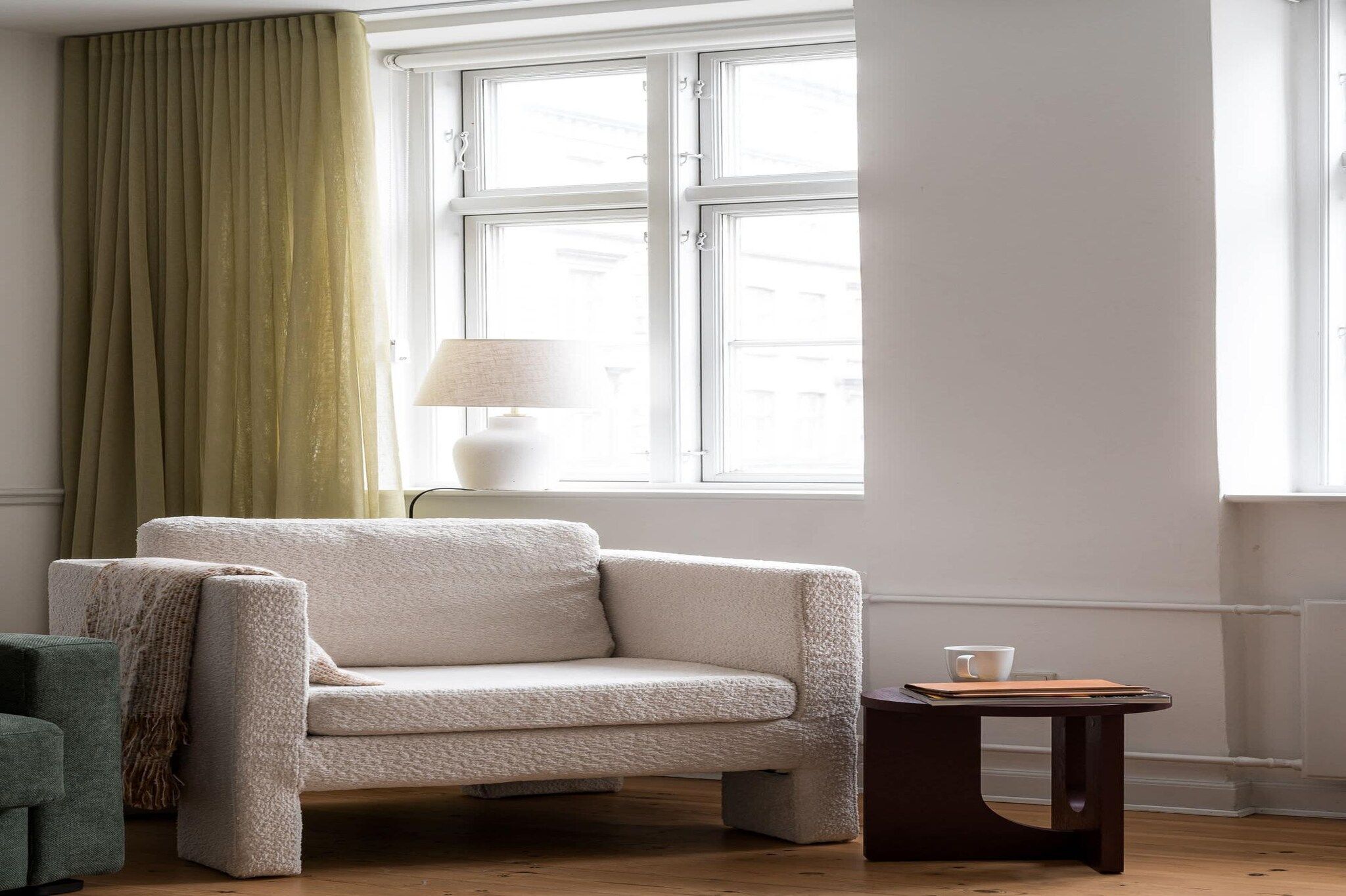 Ein Zimmer mit einer Couch, einem Tisch, einer Lampe und einem Vorhangfenster.