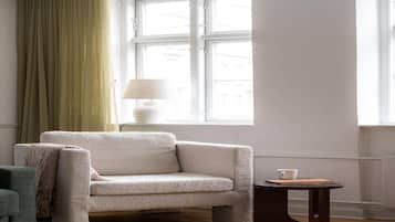 Ein Zimmer mit einer Couch, einem Tisch, einer Lampe und einem Vorhangfenster.